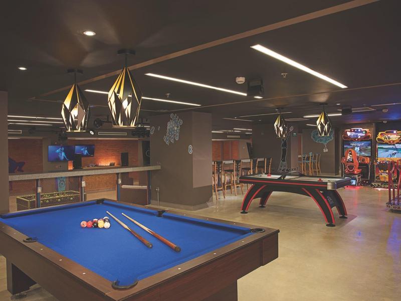 Sala giochi moderna con tavolo da biliardo, calcetto, macchine arcade e illuminazione d'atmosfera.