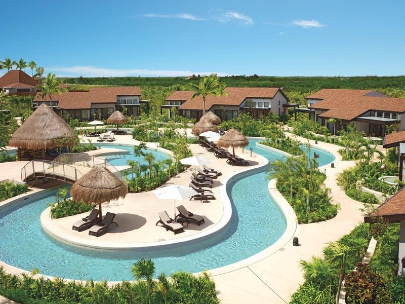 Resort con piscina tortuosa, lettini, ombrelloni di paglia e ville circostanti.