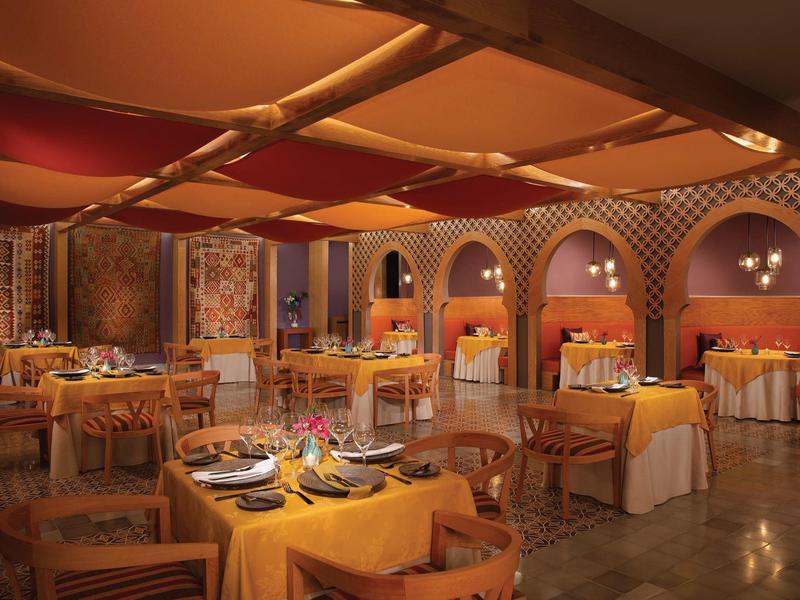 Ristorante d'hotel elegante con luci calde, mobili in legno e tavoli colorati.