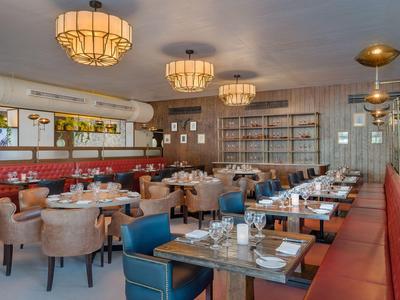 Ristorante moderno in hotel con tavoli, poltrone, sedute rosse e lampade da soffitto distintive.