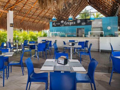 Ristorante all'aperto con sedie e tavoli blu sotto un tetto di paglia.