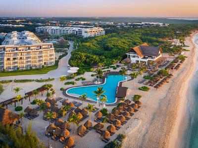 Resort con piscina, lettini e palme su una spiaggia sabbiosa tranquilla al tramonto.