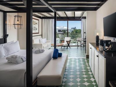 Camera d'hotel moderna con letto a baldacchino, TV, zona salotto e vista sulla terrazza.