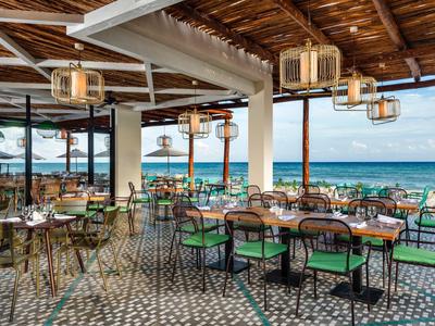 Offenes Restaurant mit gemustertem Boden, Holzdecke und Meerblick unter blauem Himmel.