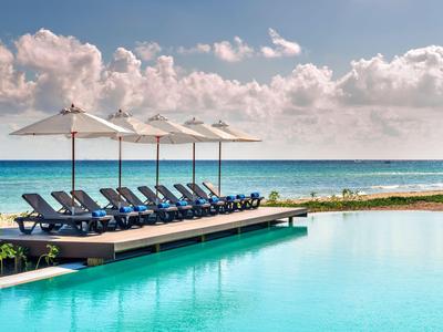 Bazén s lehátky a slunečníky u moře pod zataženou oblohou.