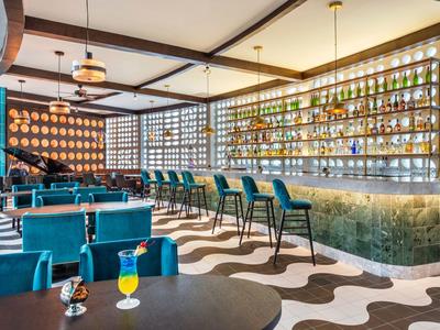 Bar hotel moderna con legno di teak, sgabelli blu e bevande colorate in un ambiente elegante.