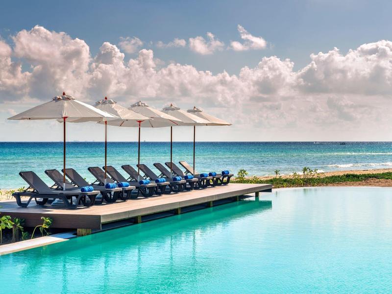 Piscina con lettini e ombrelloni con vista sul mare sotto un cielo nuvoloso.