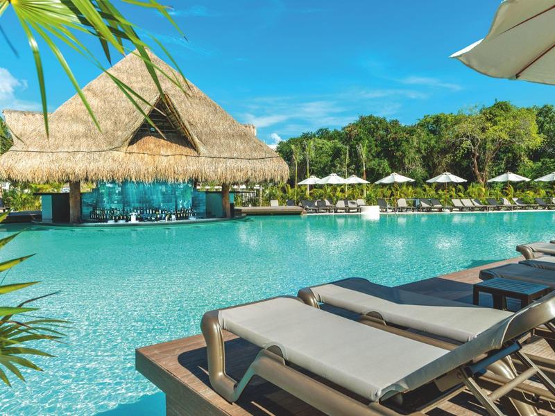 Area piscina di lusso con lettini e bar con tetto di paglia sotto cielo azzurro