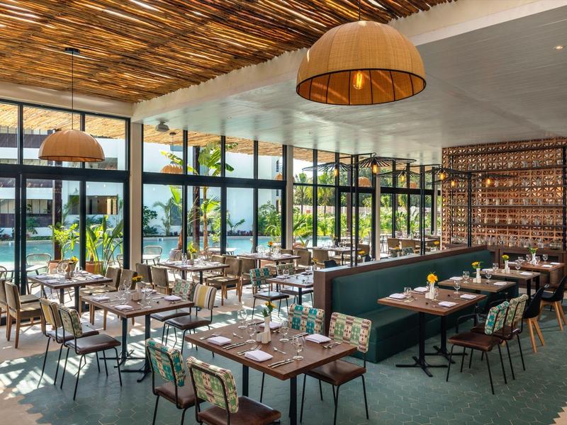 Ristorante luminoso con soffitto in legno, arredi moderni e grandi finestre con vista sul verde.