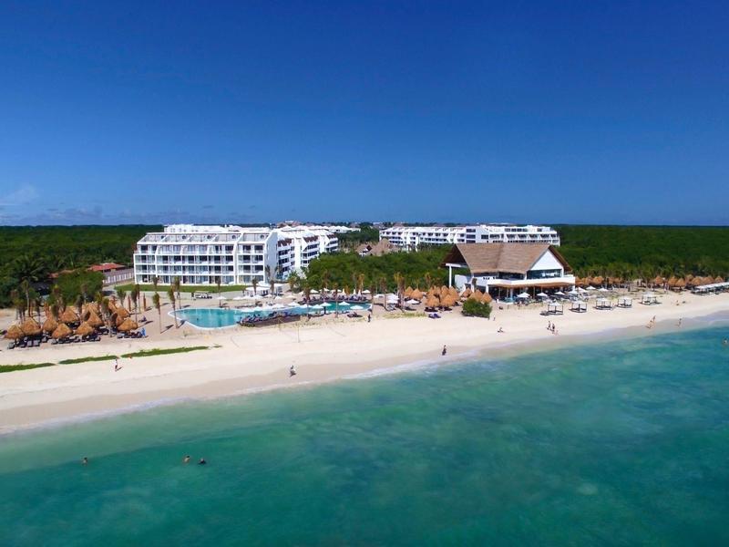 Spiaggia di sabbia bianca con mare cristallino e hotel sullo sfondo sotto un cielo azzurro.