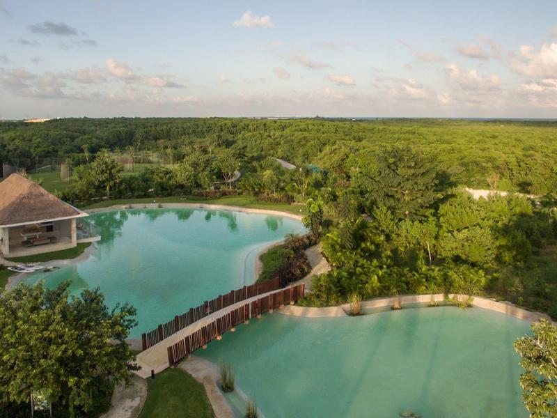 Deux grandes piscines naturelles entourées d'une végétation luxuriante et d'une forêt sous un ciel partiellement nuageux.