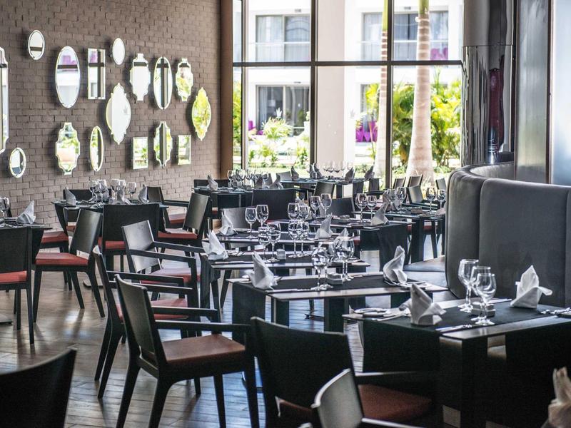 Salle à manger élégante d'hôtel avec mobilier noir, miroirs ronds et grandes fenêtres.