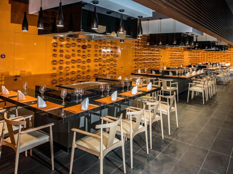 Restaurant moderne avec des chaises en bois, des tables noires et un mur décoratif orange.