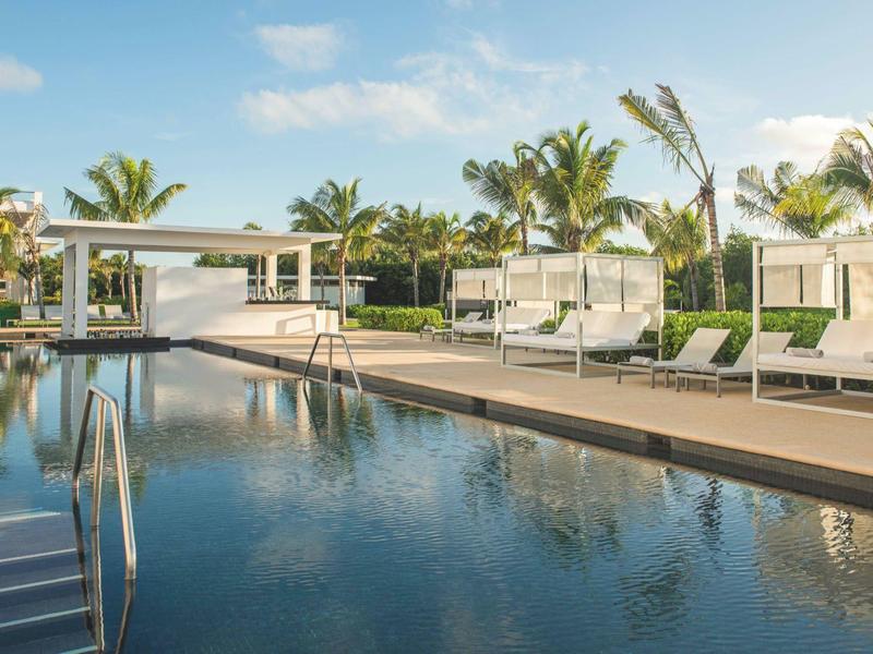 Piscine extérieure luxueuse avec chaises longues et palmiers sous un ciel bleu.