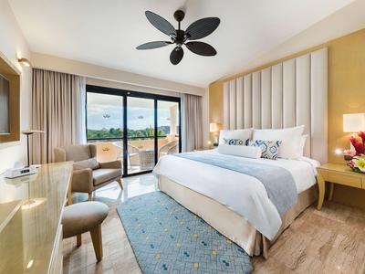 Modern hotel room with large bed, balcony, and sea view.