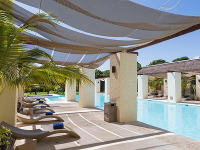 Piscina all'aperto con lettini e pergolato ombreggiante in un hotel tropicale.