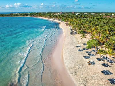 Long white sandy beach with palm trees and umbrellas by the turquoise sea.