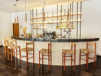 Bar moderno con sgabelli in legno e lampade sospese in uno spazio luminoso.