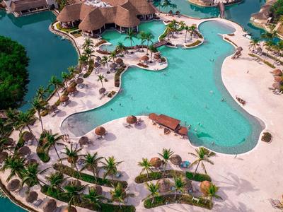 Piscina turchese a forma libera circondata da sabbia bianca e palme.
