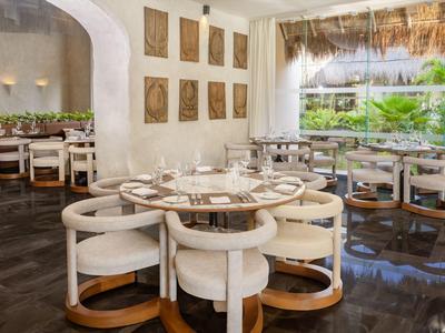 Sala ristorante elegante con tavoli rotondi in legno e grandi finestre luminose.