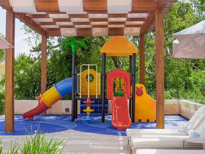 Area giochi colorata all'aperto sotto pergolato vicino a lettini e ombrellone.