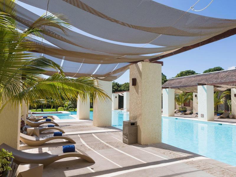 Piscina all'aperto con lettini e pergolato ombreggiante in un hotel tropicale.