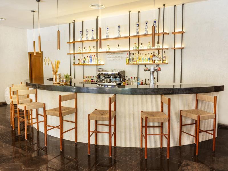 Bar moderno con sgabelli in legno e lampade sospese in uno spazio luminoso.