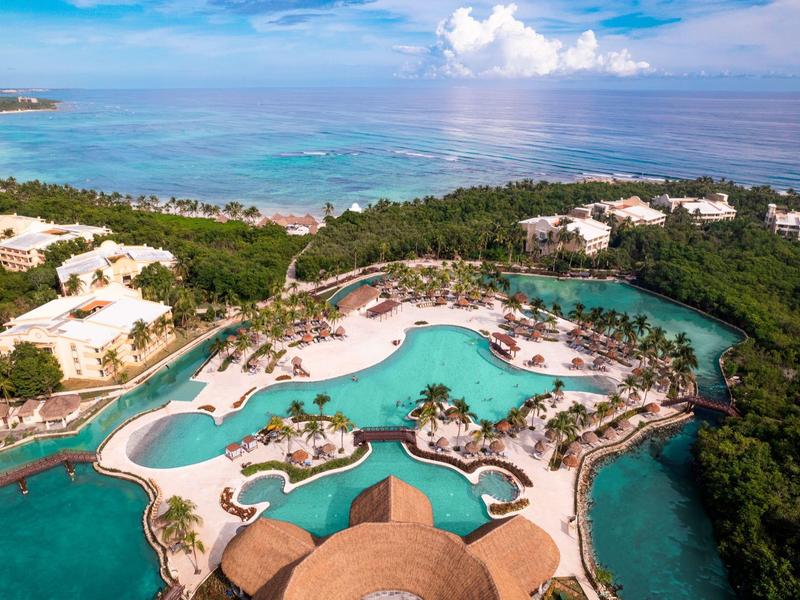 Vista aerea di una località turistica tropicale con piscine, spiagge e foresta lussureggiante.