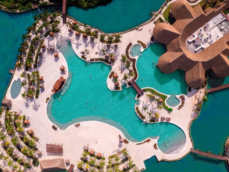 Vista aerea di una piscina complessa circondata da palme e edifici moderni vicino all'acqua.