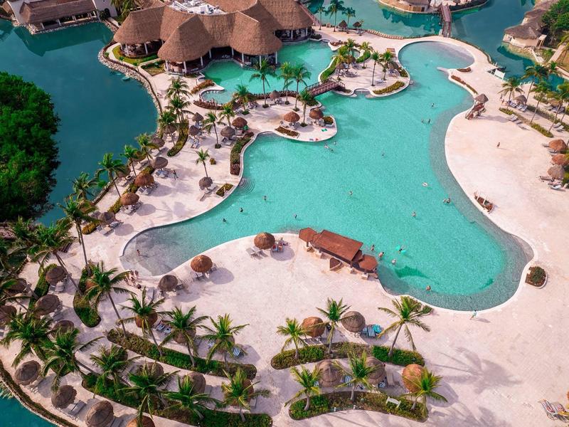 Piscina turchese a forma libera circondata da sabbia bianca e palme.