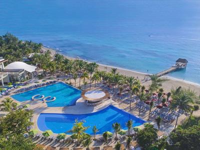 Gran piscina del hotel con palmeras en la playa con vistas al mar azul.