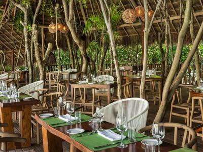 Ristorante all'aperto con sedie in legno e tavoli apparecchiati in un ambiente naturale con piante.
