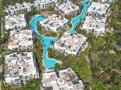 Vista aerea di edifici di hotel bianchi intorno a una piscina tortuosa in un resort tropicale.