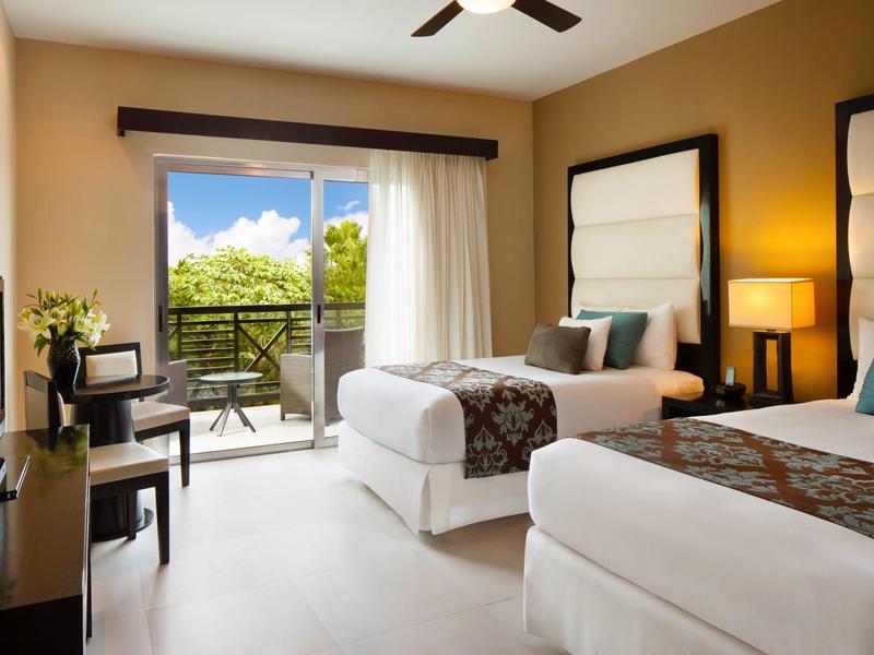 Camera d'hotel luminosa con due letti singoli, balcone e arredi moderni.