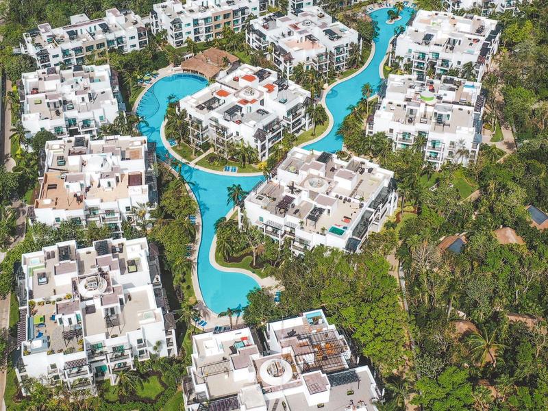 Vista aerea di edifici di hotel bianchi intorno a una piscina tortuosa in un resort tropicale.