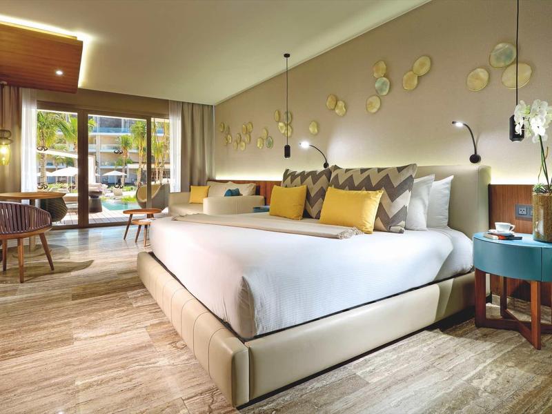 Camera d'hotel moderna con letto grande, zona salotto e balcone con vista sul verde.