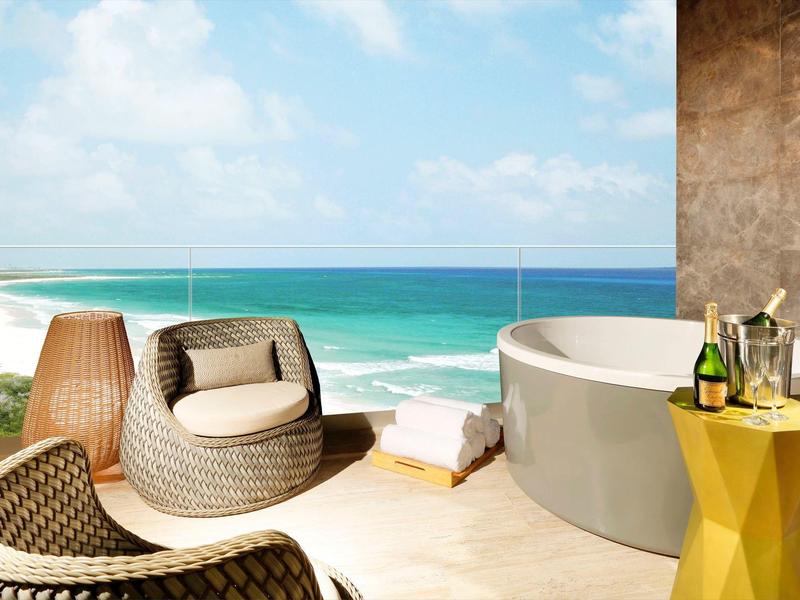 Terrazza di lusso con vasca idromassaggio, sedie e vista sull'oceano sotto un cielo azzurro.