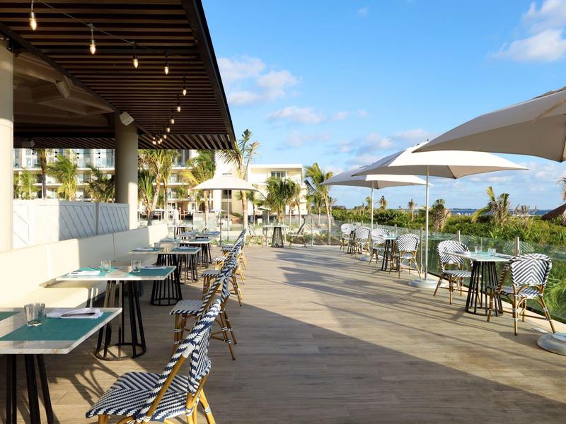 Ristorante all'aperto con tavoli, sedie e ombrelloni sotto un cielo azzurro.
