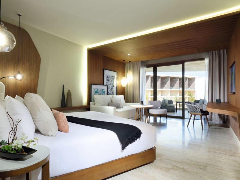 Camera d'hotel moderna con letto grande, zona salotto e accesso al balcone con mobili da esterno.