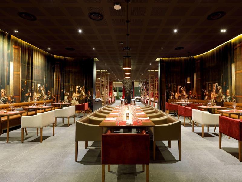 Ristorante elegante con soffitto scuro, grandi dipinti e sedute moderne dai colori caldi.