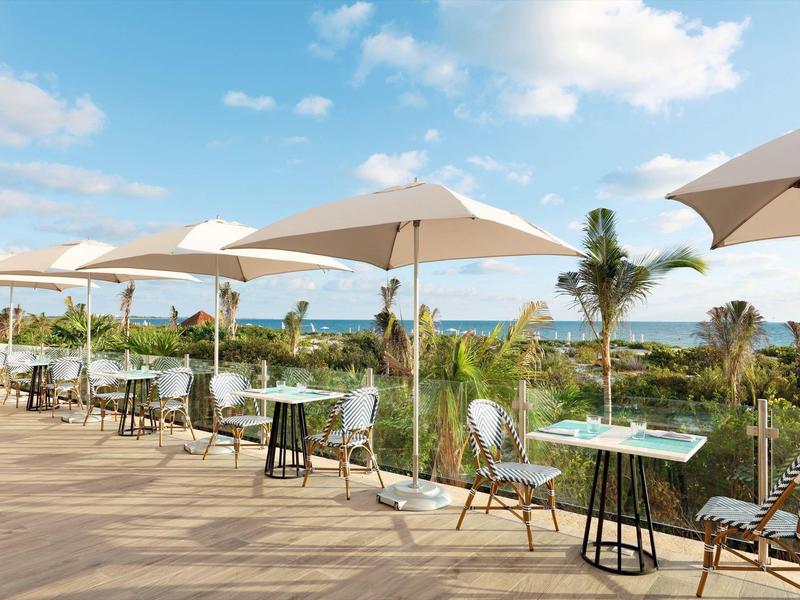 Terrazza con tavoli, sedie e ombrelloni con vista su palme e mare