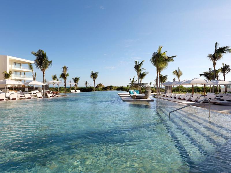 Grande piscina con acqua limpida, lettini e palme in un resort alberghiero.