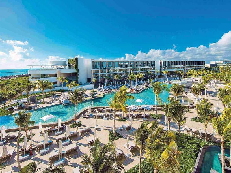 Resort di lusso con piscina a laguna, palme e lettini sulla spiaggia sotto un cielo azzurro.