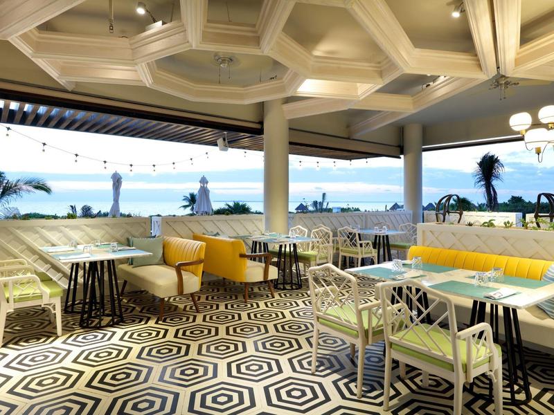 Area lounge aperta dell'hotel con arredi colorati e vista sul mare al tramonto.