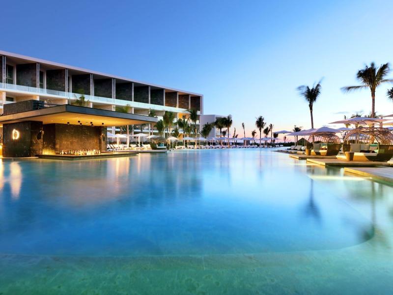 Piscina moderna dell'hotel al tramonto con area lounge e palme.