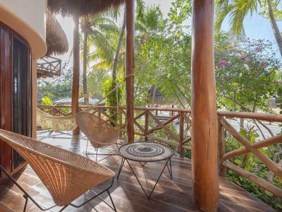 Gemütliche Veranda mit Rattanstühlen und tropischer Gartenansicht in einer Hotelanlage.