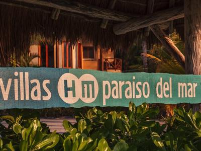 Panneau en bois indiquant 'villas Hm paraiso del mar' devant un chalet en bois avec des plantes