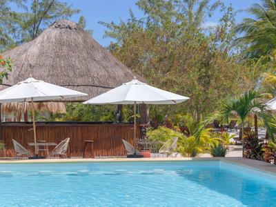 Ein Pool vor einem strohgedeckten Restaurant mit weißen Sonnenschirmen und Palmen.