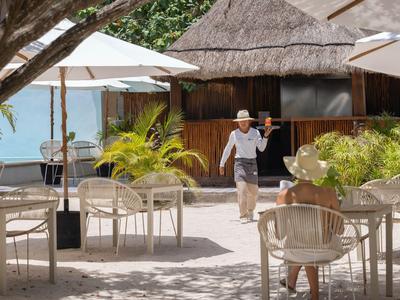 Außenterrasse eines Hotels mit Holzbungalow, Sonnenschirmen und tropischer Vegetation am Wasser.