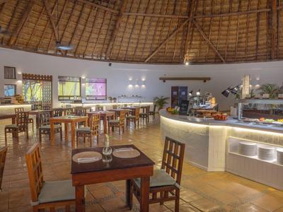 Restaurantinterieur mit Holzstühlen, gedeckten Tischen und Buffetbereich unter einer runden Strohdachdecke.
